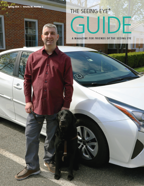 The cover of The Guide Spring 2024 shows Seeing Eye graduate Kyle Street with his Seeing Eye dog, a black Labrador/golden retriever cross, standing in front of a parked white car.