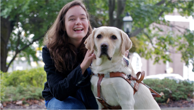 A Seeing Eye graduate laughs as she holds her Seeing Eye dog, a yellow Labrador retriever.