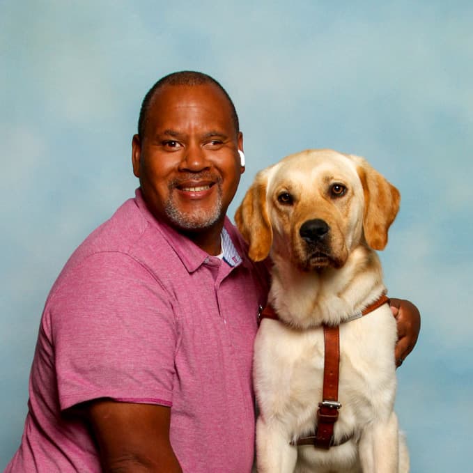 Seeing Eye graduate Cedric smiles with his arm around his yellow Lab/golden retriever cross Seeing Eye dog.