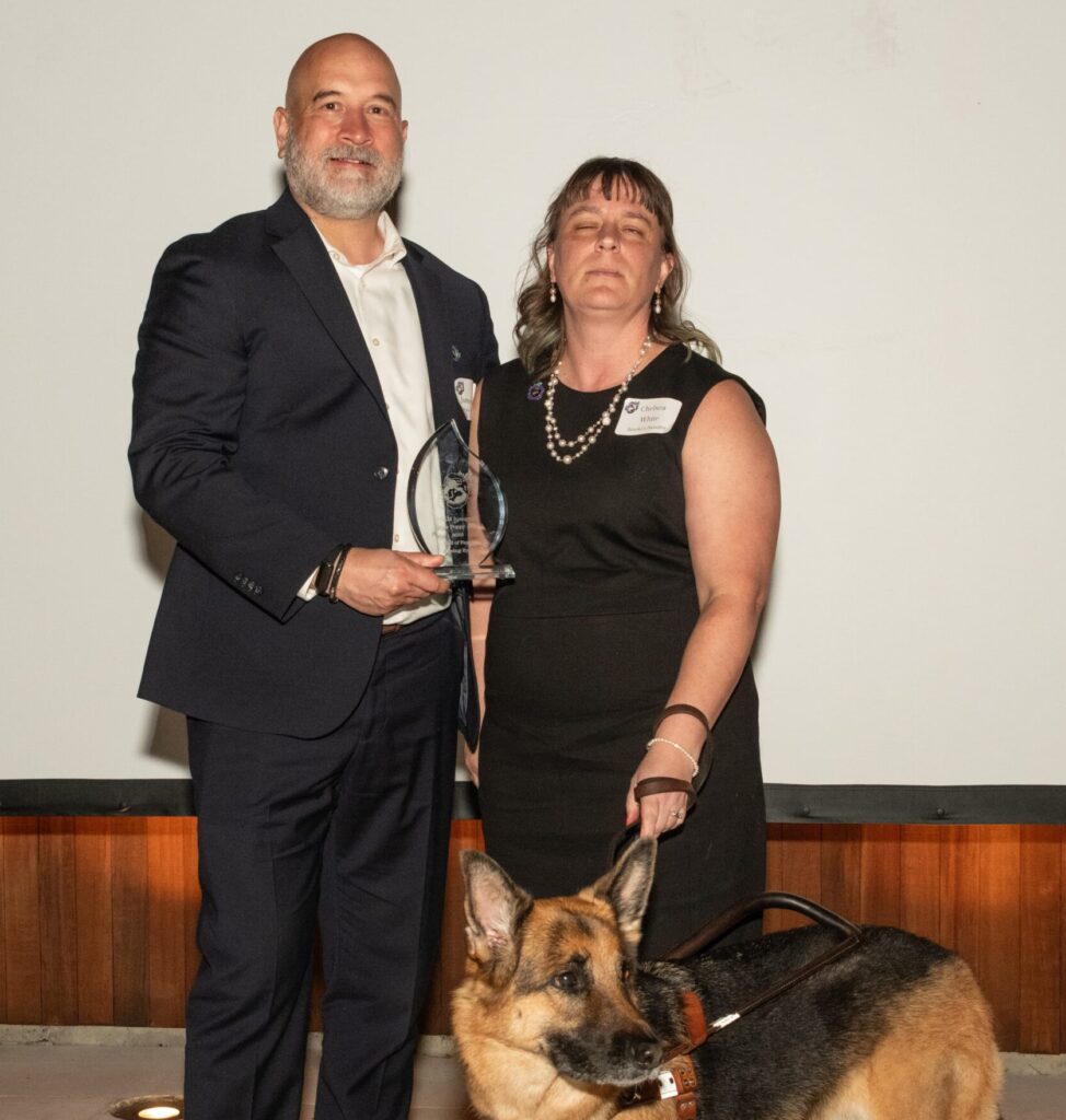 Seeing Eye Chief Financial and Operating Officer James Hands holding an award and standing beside Seeing Eye Outreach Specialist Chelsea White and her German shepherd Seeing Eye dog, Brooke.