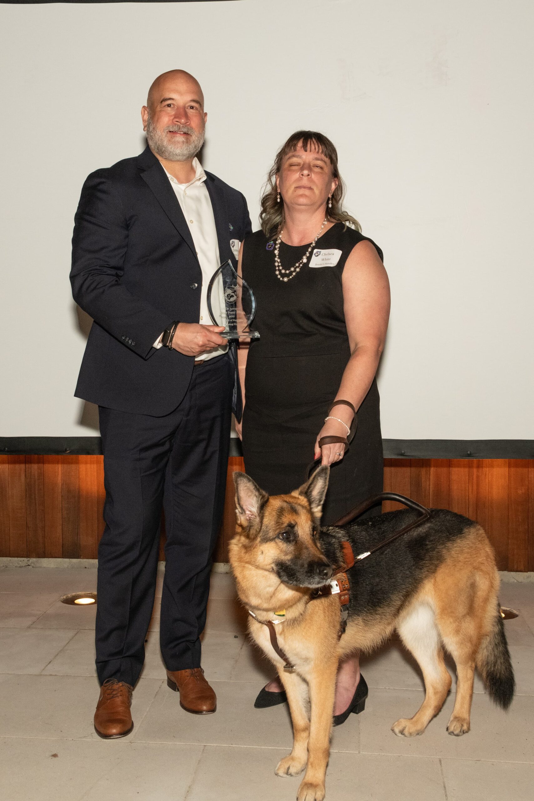 Seeing Eye Chief Financial and Operating Officer James Hands holding an award and standing beside Seeing Eye Outreach Specialist Chelsea White and her German shepherd Seeing Eye dog, Brooke.