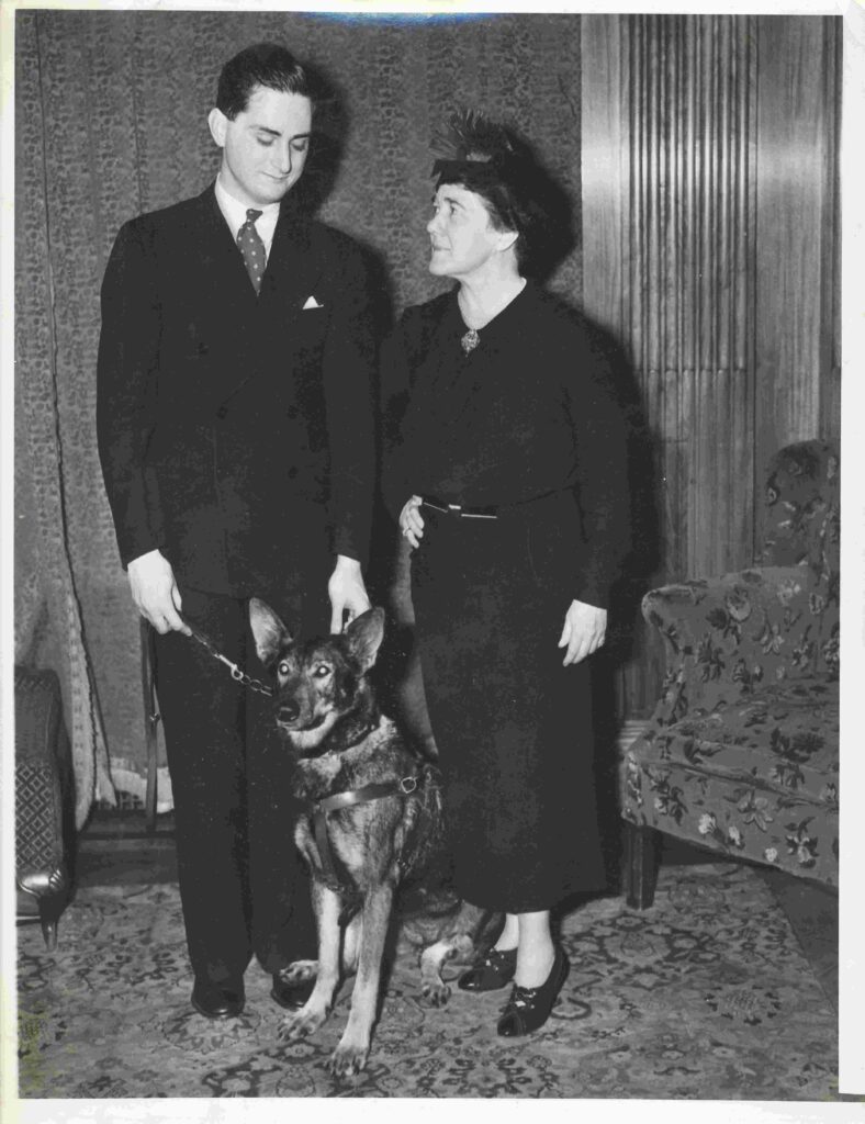 Black and white archival photo of Seeing Eye cofounders Morris Frank and Dorothy Harrison Eustis standing together with Buddy the first Seeing Eye dog.