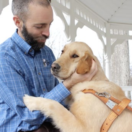 A Seeing Eye instructor pets a golden retriever, in harness.