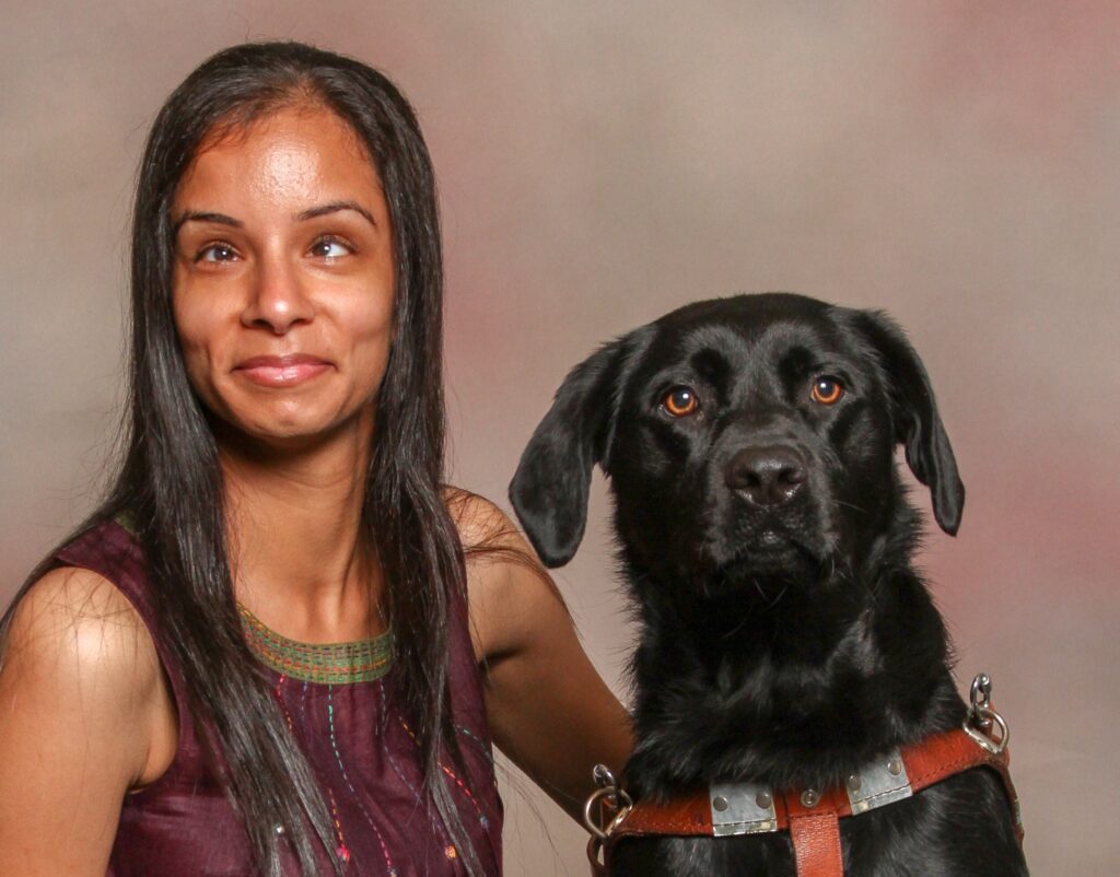 A woman with her arm around a black Labrador retriever.