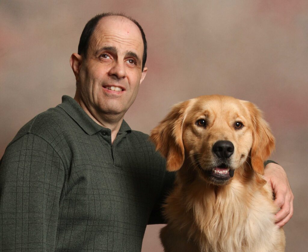 A man with his arm around a golden retriever.