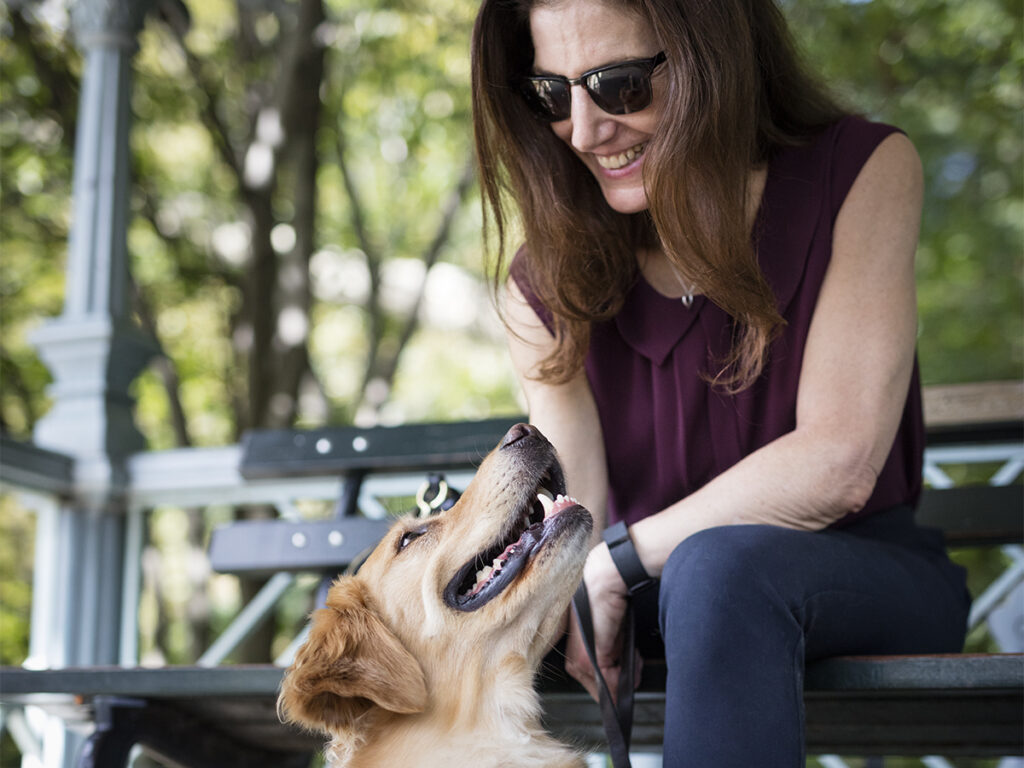 A Seeing Eye graduate sits on a bench and smiles at her Seeing Eye dog, a golden retriever.