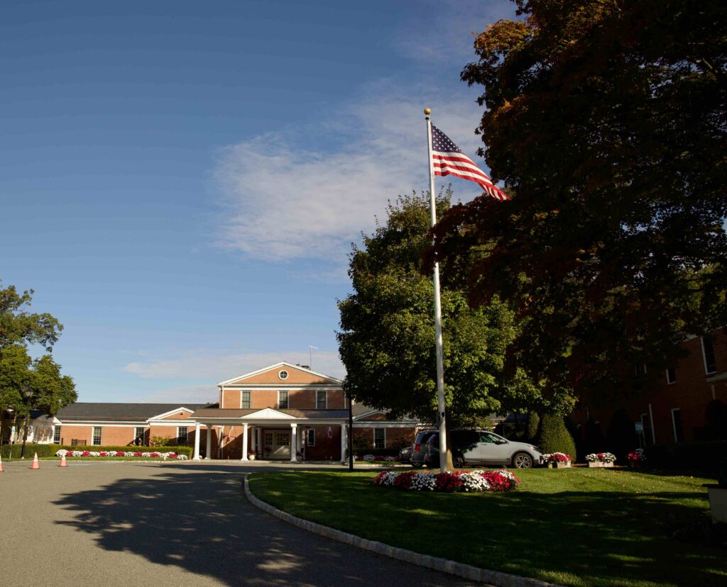 An American flag flies on a large flagpole before the main campus building with a red brick exterior.