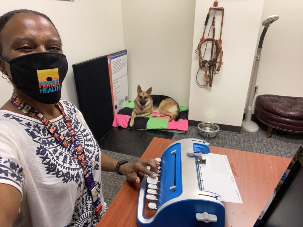 A Seeing Eye graduate types on a brailler as her Seeing Eye dog, a German shepherd, watches from her dog bed.