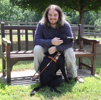 A Seeing Eye graduate hugs his Seeing Eye dog, a black Labrador/golden retriever cross, as he sits on a bench.