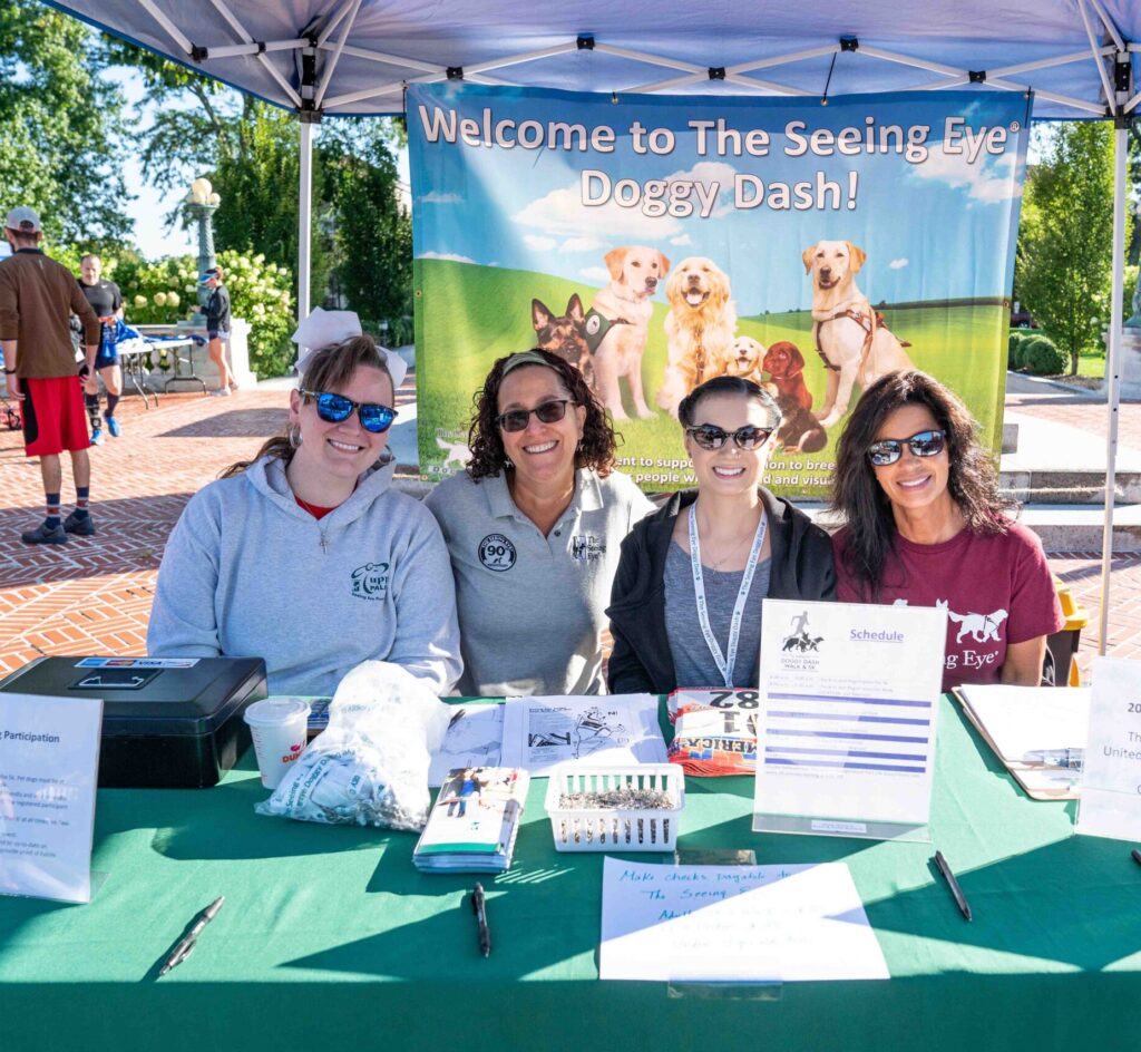 Four smiling women seated at a registration table for a fundraising walk.