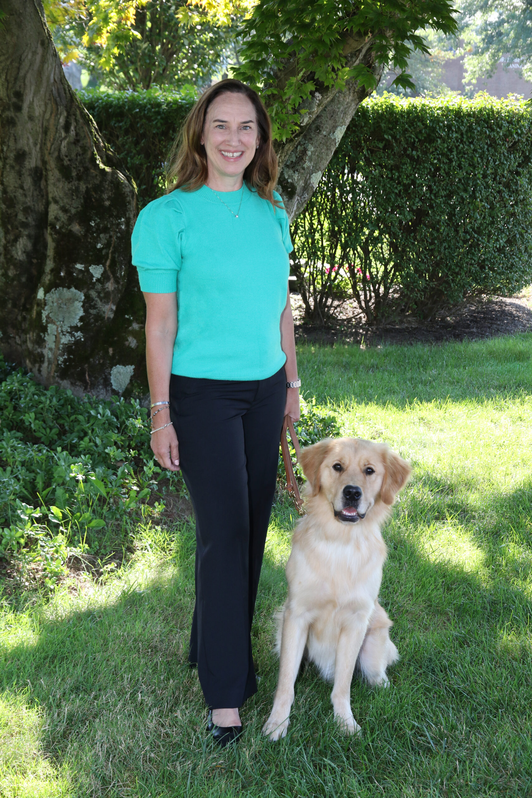 Karen Leies on The Seeing Eye campus with a golden retriever, in harness, sitting at her side.