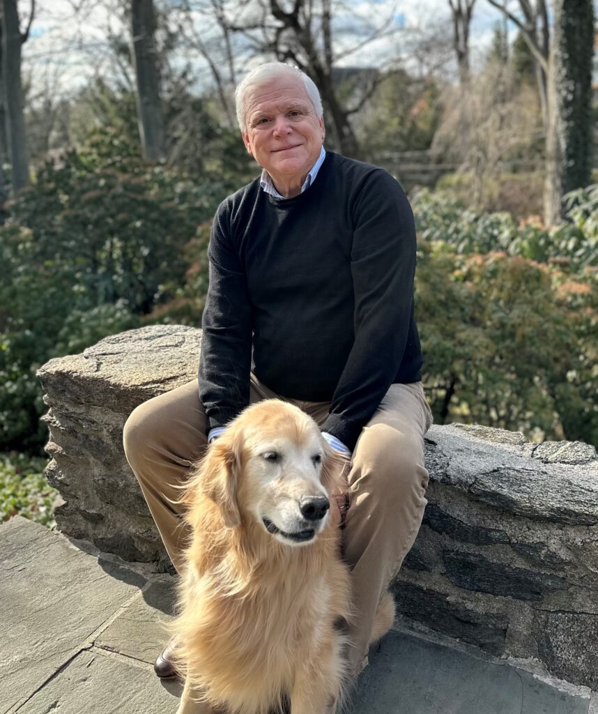 Brad Hart sitting on a wall with a golden retriever seated on the ground in front of him.