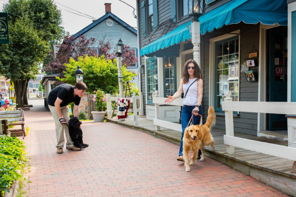 A young man bends down to restrain his large dog as a guide dog team exits a local shop.