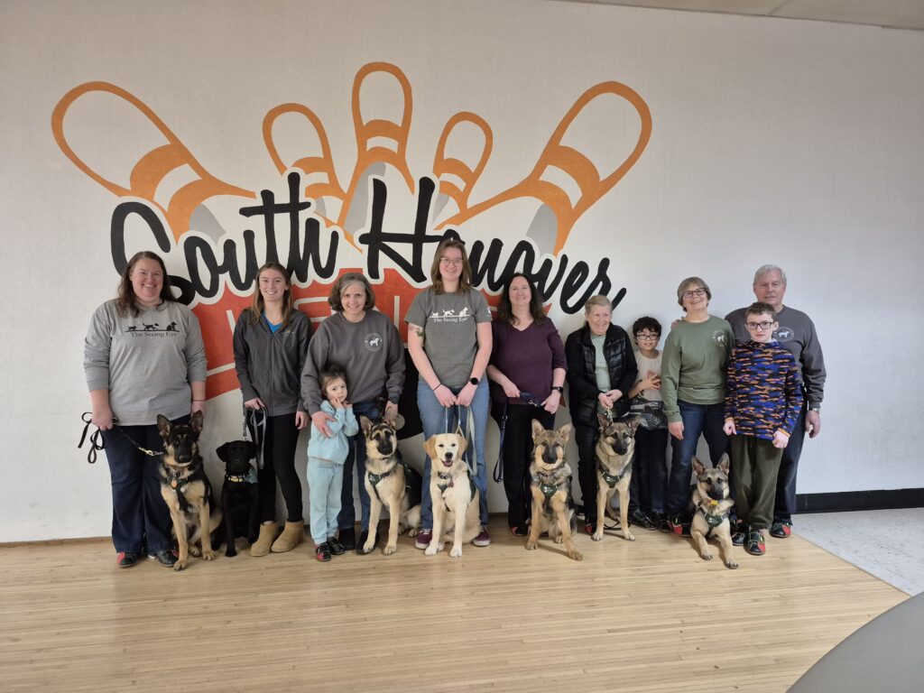 Eleven Carroll County puppy club members stand together with five German shepherds, one black Lab and one yellow Lab, before a wall bearing the South Hanover Lanes logo.