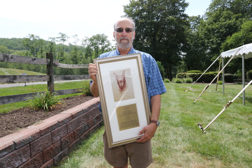 Lukas Franck, Retired, holds the Buddy Award, a framed piece with an image of Buddy, the first Seeing Eye dog, and a dedication below.