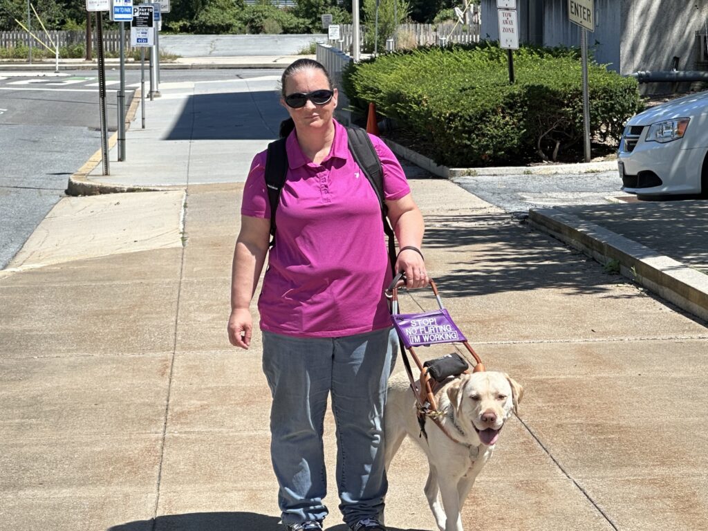 Seeing Eye graduate Milissa walks down the sidewalk during her commute to work with her yellow Lab/golden retriever cross Seeing Eye dog Ruffles.