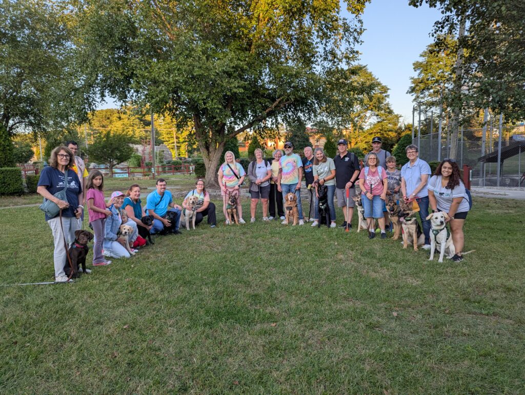 Twenty members of the Ocean County puppy raising club pose together at Swing Time Mini-Golf with the eleven puppies they are raising, which include a chocolate Lab, two yellow Labs, two black Labs, a golden retriever, and five German shepherds.