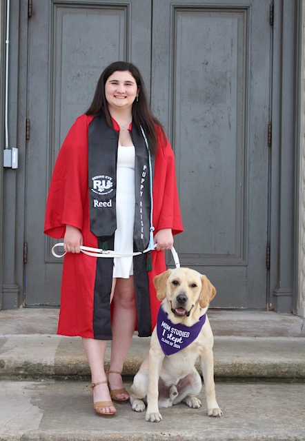 Sydnee, wearing her Rutgers graduation gown, stands with Reed, a yellow Lab golden retriever cross who wears a bandana that reads “Mom studied, I slept, Class of 2024.”