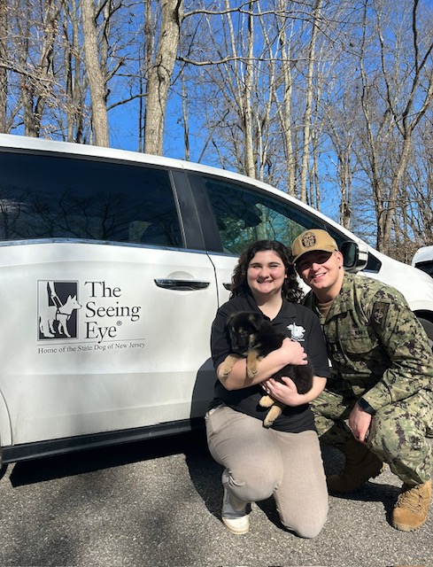 Sydnee and her husband, who wears his Army combat uniform, kneel beside a Seeing Eye van holding seven-week-old Saturn.