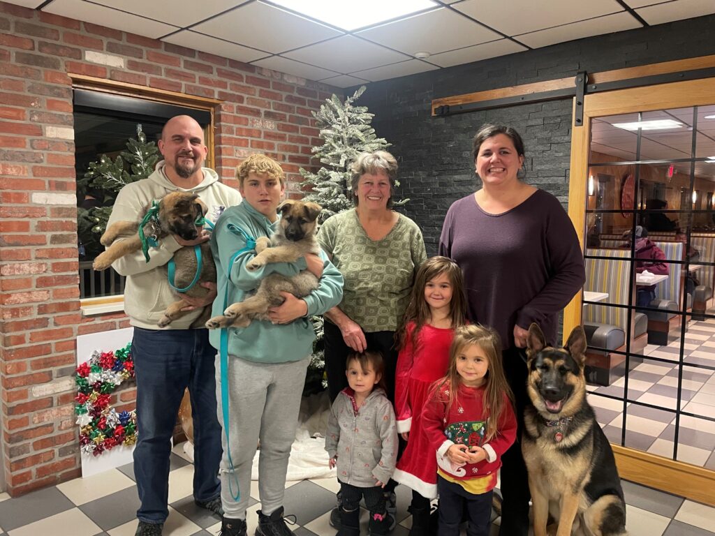 The Theurer family, Scott and his son, Marianne, and Laura and her three daughters at the Juniata County December club meeting. Scott and his son hold German shepherd puppies while the German shepherd Laura is raising sits beside her daughters.