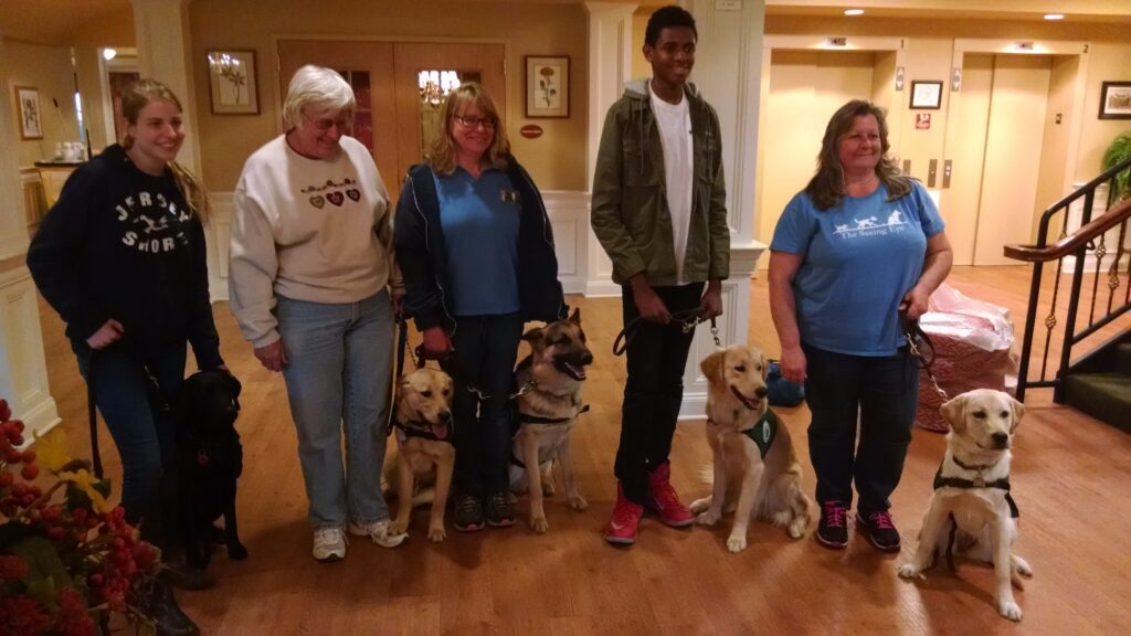 Five Seeing Eye puppy raisers, including one of the Turner’s sons, stand together with a black Lab, two yellow Labs, a German shepherd, and a golden retriever.