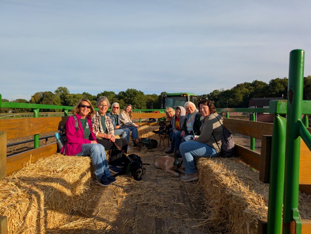 Eight Passaic County club members and their four Seeing Eye puppies, a black Lab, two German shepherds, and a yellow Lab, sit together on a hayride at a local farm.