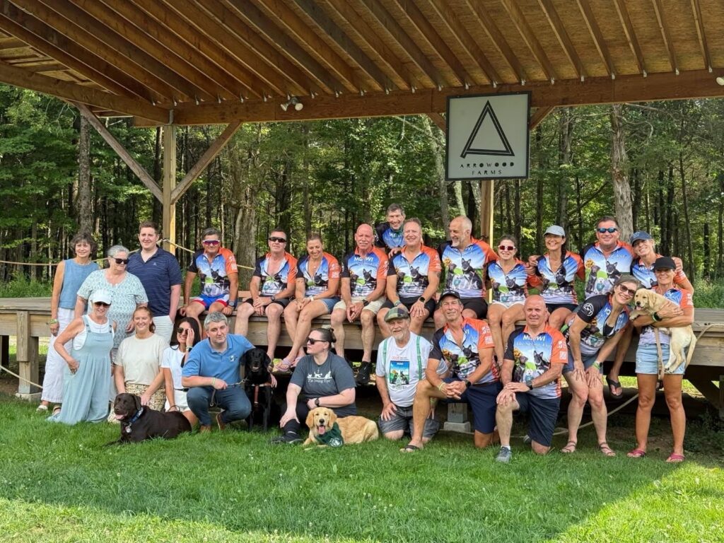 A large group of people, many wearing Seeing Eye bicycle jerseys, with Seeing Eye graduate Kyle Street and several puppy raisers in the front row.