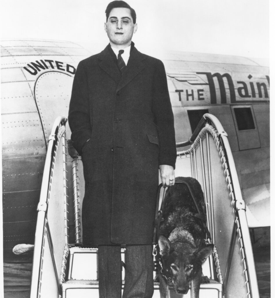 A historical black and white photo of Morris Frank and Buddy, his German shepherd Seeing Eye dog, exiting a United Airlines plane.